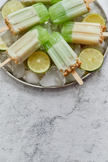 Delicious lime and cream homemade popsicles or ice creams placed with ice cubes on gray stone backdrop Flat lay top view with copy space