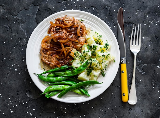 Delicious lunch pork chop creamy potatoes and green beans on a dark background top view