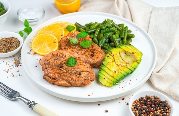 Delicious lunch with chicken steak and garnish with beans and avocado on a light background.