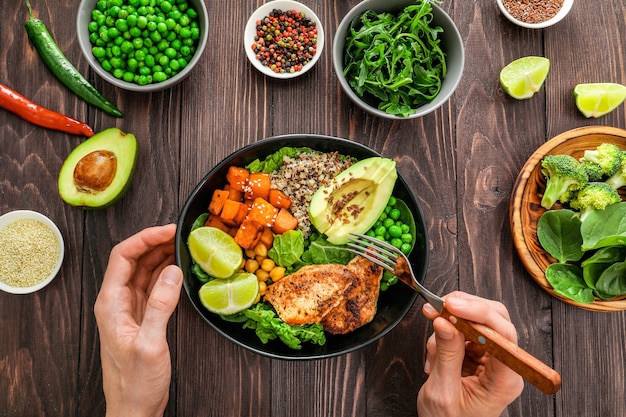 Delicious lunch with quinoa, avocado, sweat potato, fried chicken and seasoning on wooden background. Top view.