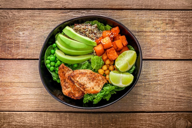 Pranzo delizioso con quinoa, avocado, patate sudate, pollo fritto e condimento su fondo di legno. vista dall'alto.