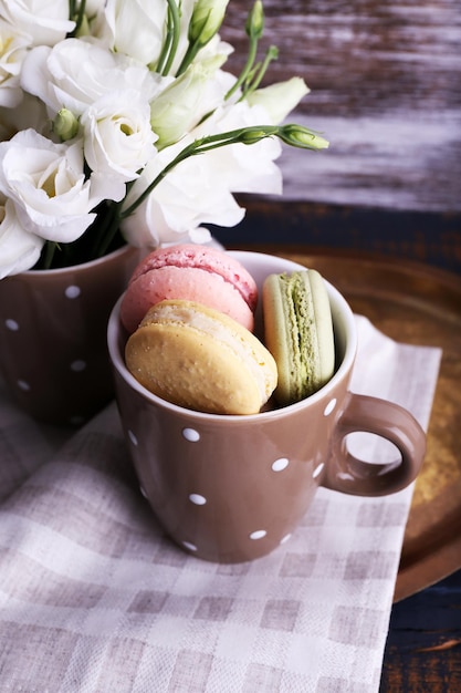 Delicious macaroon with beautiful flowers on wooden background