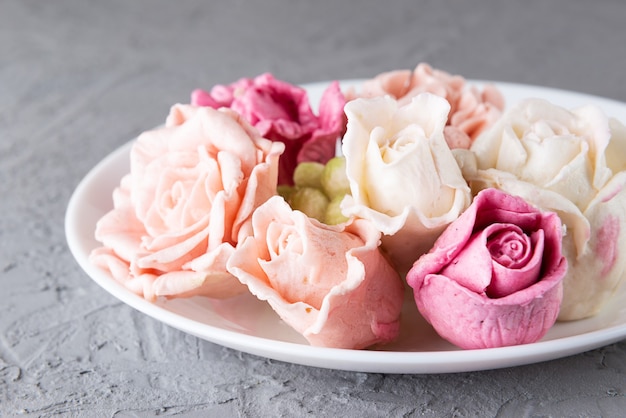 Delicious marshmallow roses on a plate on a gray background.