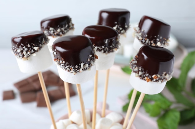 Delicious marshmallows covered with chocolate on sticks closeup