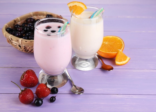 Delicious milk shakes with orange and blackberry on wooden table closeup