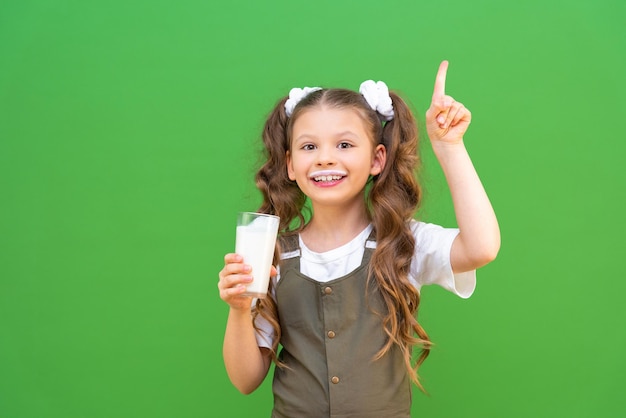 かわいい子供の手による朝食用のおいしいミルクセーキカクテルを持った女の子が広告を指しています子供の体への乳製品の利点