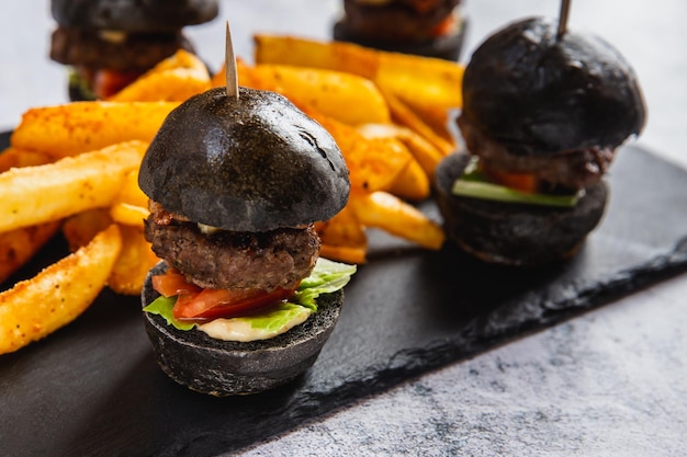 Delicious mini black burgers with beef tomato cheese served with french fries on black table