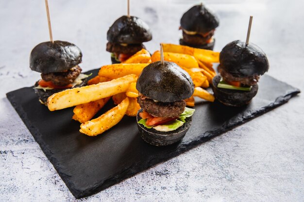 Foto deliziosi mini hamburger neri con formaggio al pomodoro di manzo servito con patatine fritte sul tavolo nero