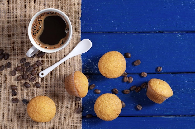 Delicious mini muffins and cup of coffee on blue wooden table, top view