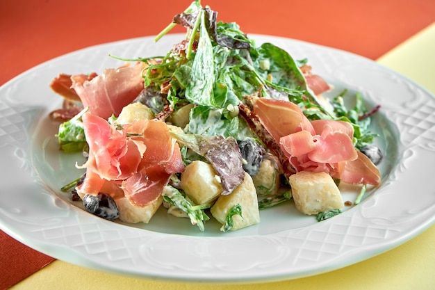 Delicious mix salad with jamon and pear in a white plate on bright colored surface