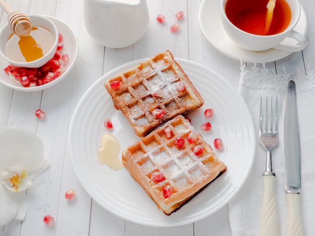 Delicious mouth-watering Viennese waffles with honey and pomegranate seeds on a white plate