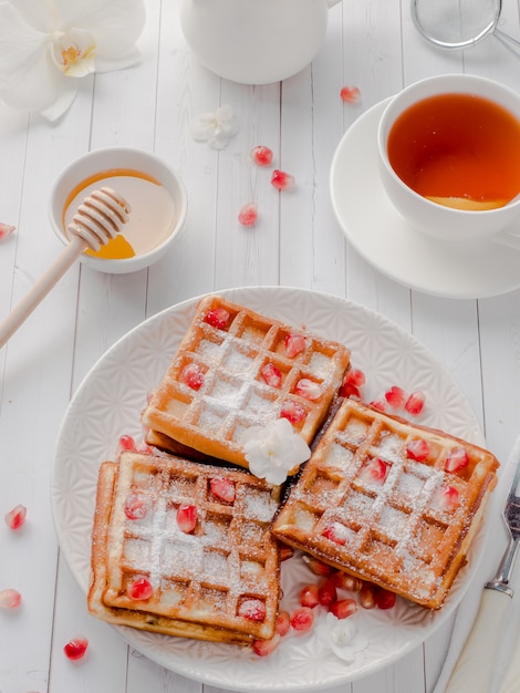 Delicious mouth-watering Viennese waffles with honey and pomegranate seeds on a white plate