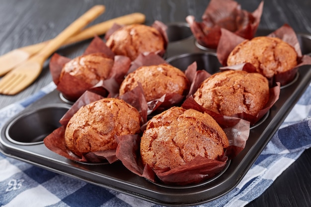 Delicious muffins in a steel baking tray with kitchen towel on a black wooden table