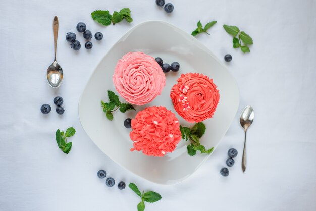 Delicious multi-colored cupcakes on a white plate on a white background.