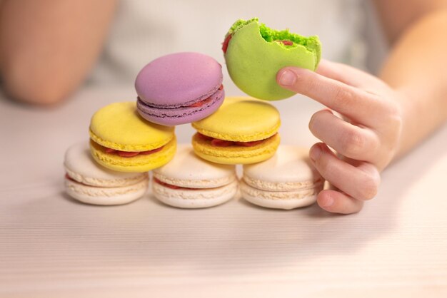 Delicious multicolored cookies in the hands of a child macaron kid girl bites pistachio macaron