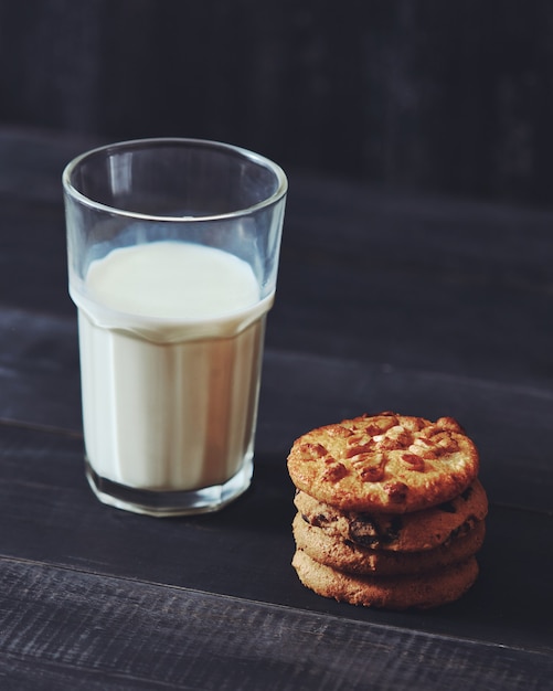 Delicious natural cakes, baked from oatmeal - chocolate, nut, raisins with a glass of milk on a black wooden table. Healthy vegan food eating.