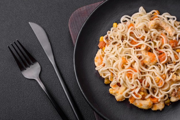 Delicious noodles with chicken and vegetables or udon on a black ceramic plate