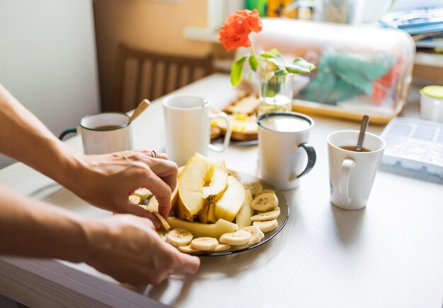 A delicious nutritious breakfast with tea and coffee, cut into pieces melon and banana, fresh toast with butter and nuts are on table waiting for company or family in cozy home kitchen in the morning