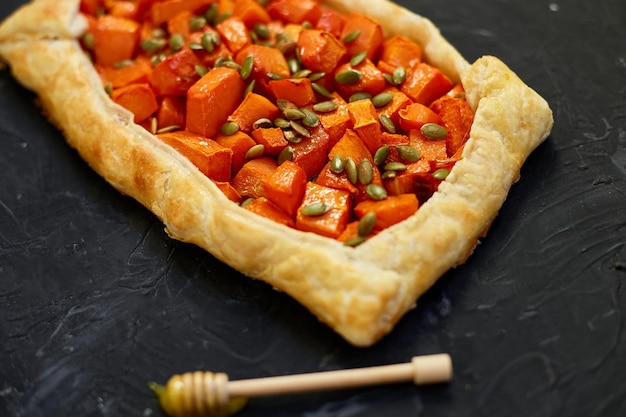 Delicious open pumpkin pie on black background with honey and thyme