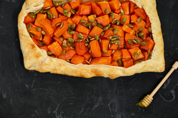 Delicious open pumpkin pie on black background with honey and thyme