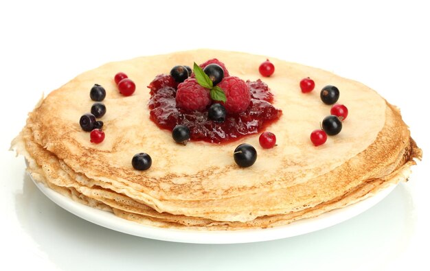 Вкусные блины с ягодами и джемом на тарелке, изолированной на белом