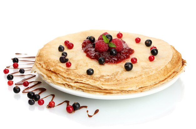 Вкусные блинчики с ягодами и вареньем на тарелке, изолированной на белом