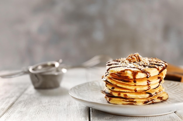 Deliziose frittelle con sciroppo di cioccolato e noci su tavola di legno bianca