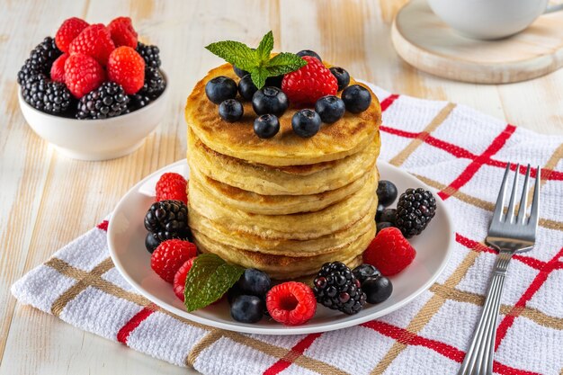 Delicious pancakes with fresh berries on white wooden table.