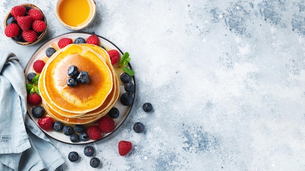 Delicious pancakes with fresh blueberries raspberry and maple syrup or honey on a dark background