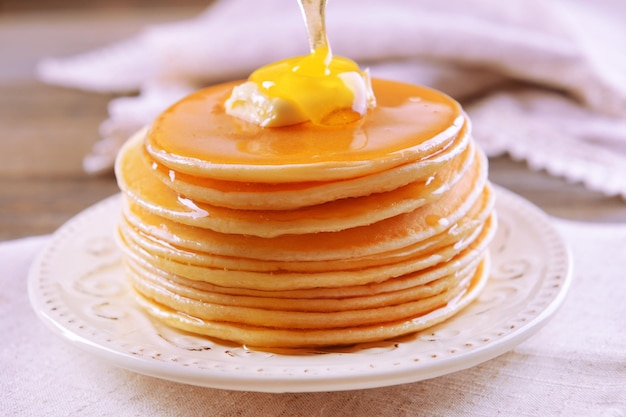 Delicious pancakes with honey on plate on table closeup