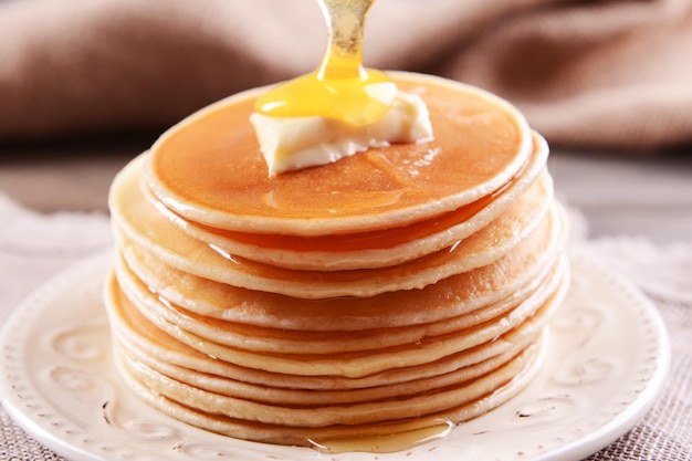 Delicious pancakes with honey on plate on table closeup