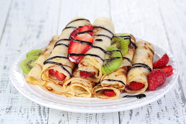 Вкусные блинчики с клубницей и шоколадом на тарелке на столе