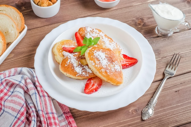 Deliziose frittelle con fragole e zucchero a velo su un piatto bianco su un piatto di legno scuro