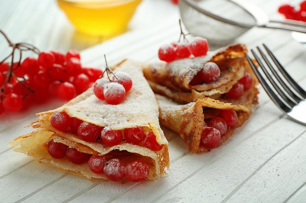 Delicious pancakes with viburnum and sugar powder on wooden board