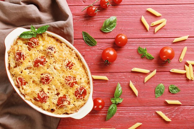 Foto deliziosa pasta al forno in ciotola di ceramica e tovagliolo marrone su tavolo di legno rosso