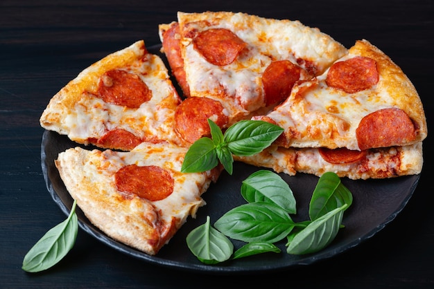 Delicious pepperoni pizza and basil on dark background