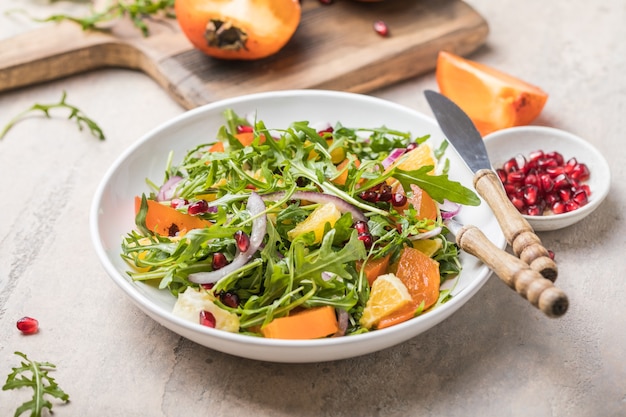 Deliziosa insalata di cachi con rucola e arancia servita sul tavolo grigio chiaro, piatto lay. spazio per il testo