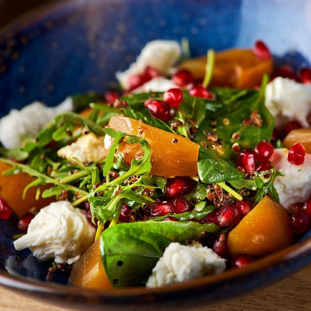 Delicious persimmon salad with pomegranate and arugula on the table serving in a restaurant menu food concept