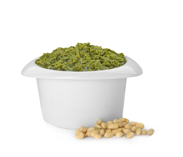 Delicious pesto sauce in bowl and pile of pine nuts isolated on white