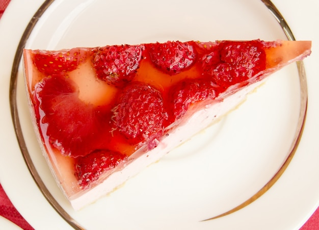 하얀 접시에 있는 맛있는 딸기 치즈케이크 조각, 빨간 체크무늬 냅킨이 있는 탁자 위에 있는 꼭대기.