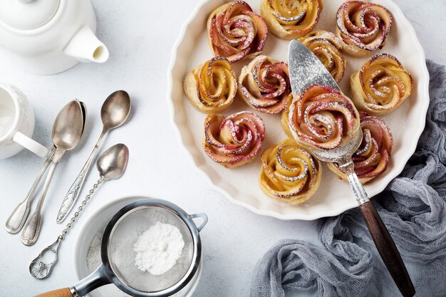 Delicious pies with an apple rose in ceramic form on a light concrete