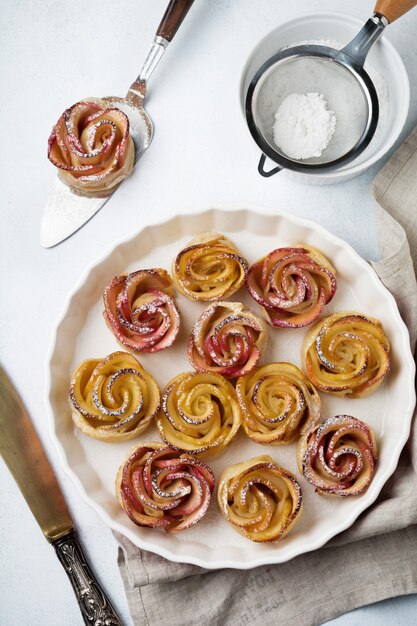 Delicious pies with an apple rose in ceramic form on a light concrete