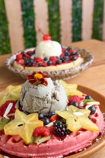Delicious pink ice cream waffle with red fruits and starfruit on wooden table