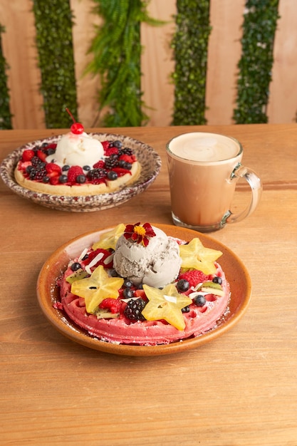 Delicious pink ice cream waffle with red fruits and starfruit on wooden table