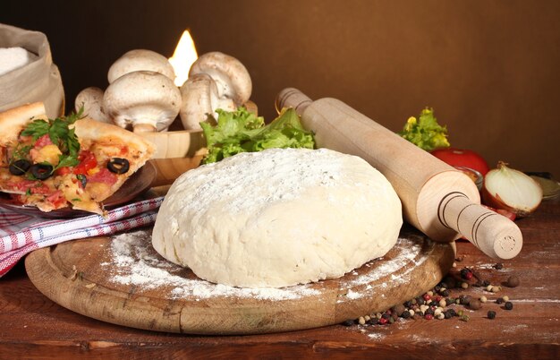 Delicious pizza dough, spices and vegetables on wooden table on brown