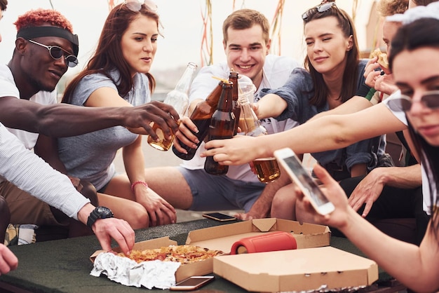 Photo delicious pizza group of young people in casual clothes have a party at rooftop together at daytime