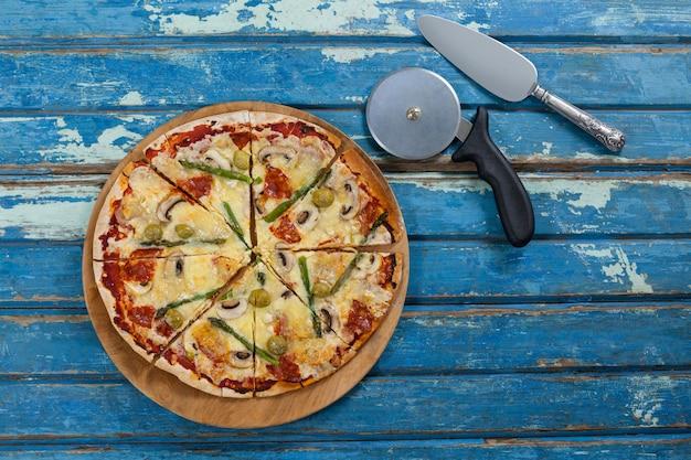 Delicious pizza served on pizza tray with cutter and knife on wooden plank