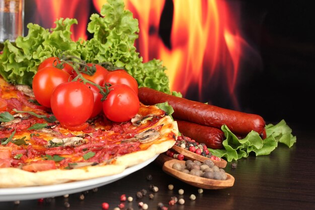 Delicious pizza and tomatoes on wooden table on flame background