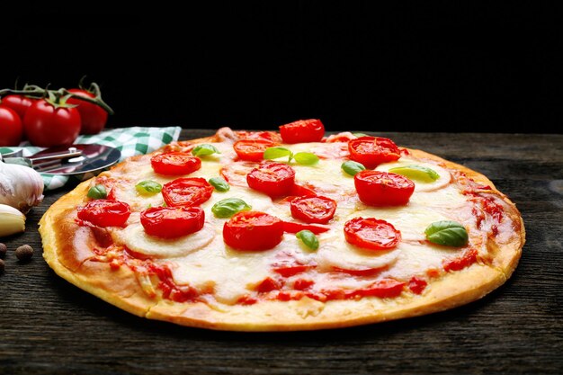 Delicious pizza with cheese and cherry tomatoes on wooden table on dark background