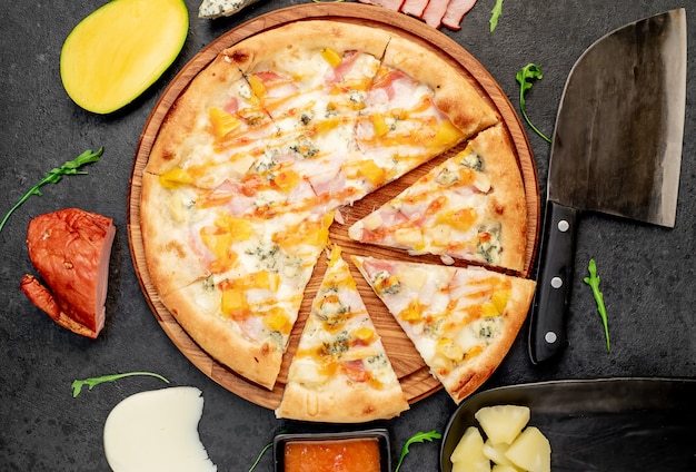 delicious pizza with ham cheese pineapple mango on a stone background